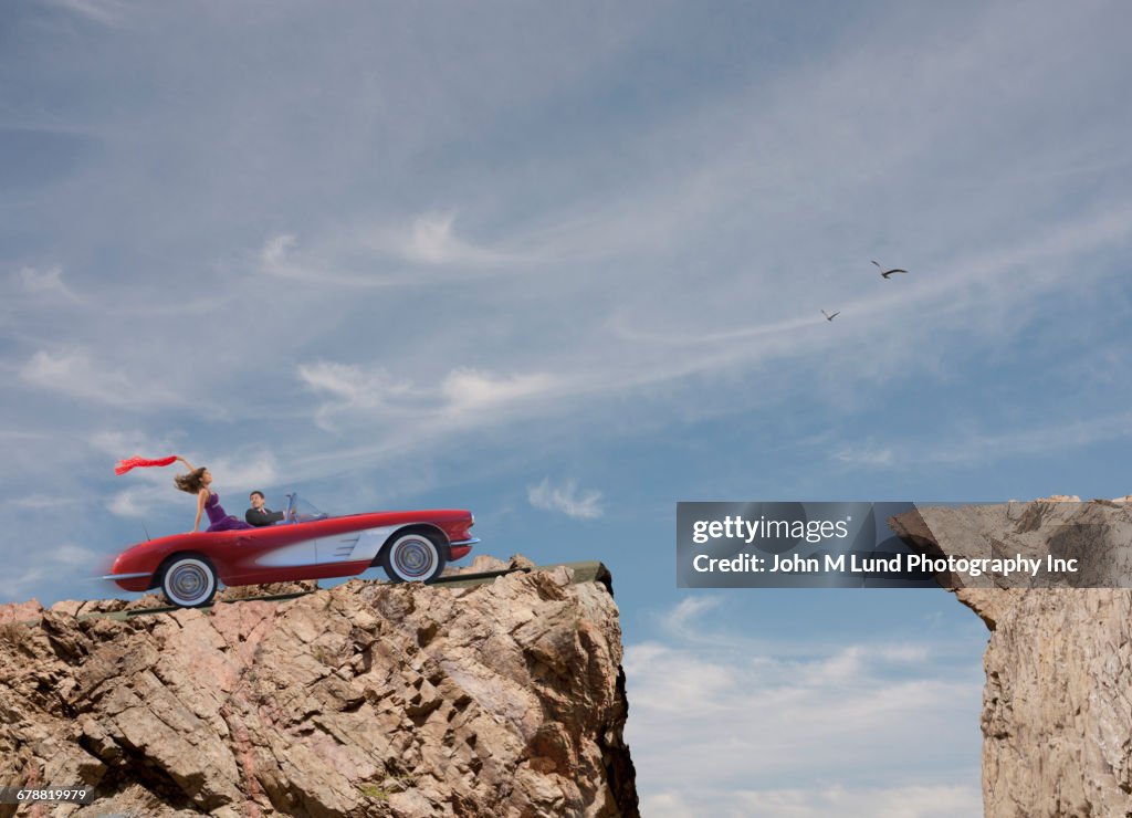 Oblivious couple driving convertible over cliff