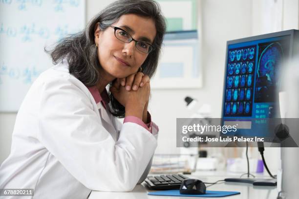 smiling hispanic radiologist posing near computer at desk - health authority stock pictures, royalty-free photos & images