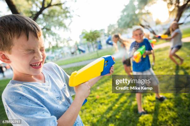 caucasian boys and girls playing with squirt guns - pistola de agua fotografías e imágenes de stock