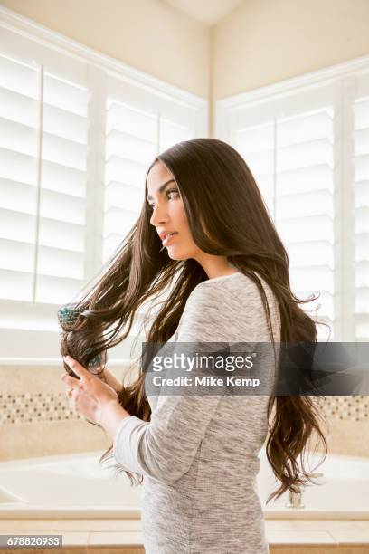 mixed race woman brushing hair in bathroom - woman brushing hair stockfoto's en -beelden