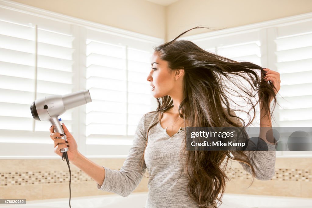 Mixed Race woman drying hair in bathroom