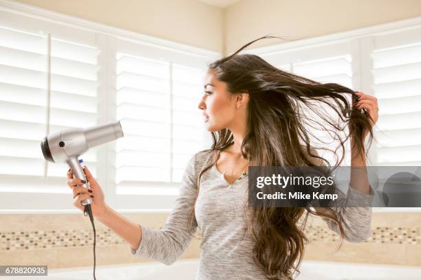 mixed race woman drying hair in bathroom - secador de pelo fotografías e imágenes de stock