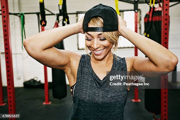 mixed race woman adjusting hat in gymnasium - close up of beautiful young blonde woman with black hat stock pictures, royalty-free photos & images