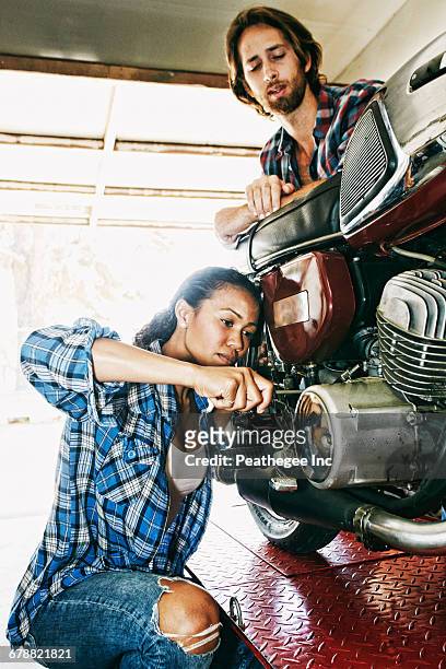 man watching woman repairing motorcycle in garage - women black and white motorcycle fotografías e imágenes de stock