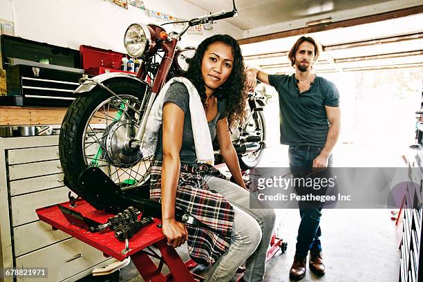 serious man and woman posing with motorcycle in garage - women black and white motorcycle fotografías e imágenes de stock