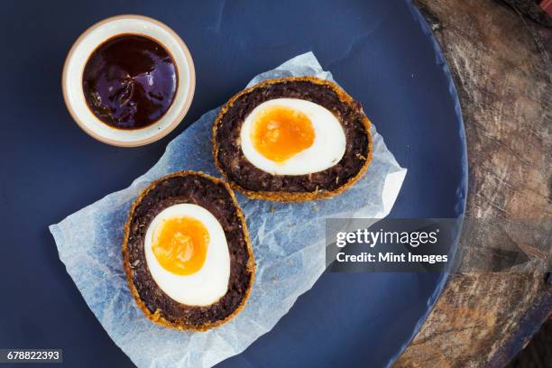 village pub food. a blue dish with a fresh made scotch egg cut in to two and a pot of sauce. - scotch egg stock pictures, royalty-free photos & images