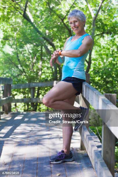 caucasian woman leaning on wooden fence checking the time - une seule femme d'âge mûr photos et images de collection