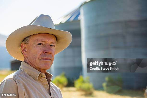 serious caucasian farmer near storage silos - cowboyhut stock-fotos und bilder