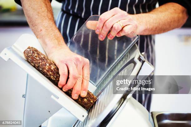 close up of a butcher wearing a striped blue apron, slicing salami with a slicer. - charcutería fotografías e imágenes de stock
