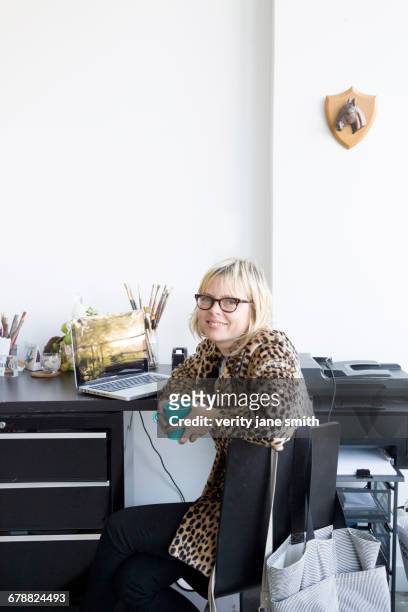 caucasian woman drinking coffee at desk with laptop - patrón de leopardo fotografías e imágenes de stock