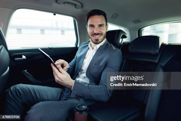 businessman in a car using digital tablet and smiling. - chauffeurs stock pictures, royalty-free photos & images