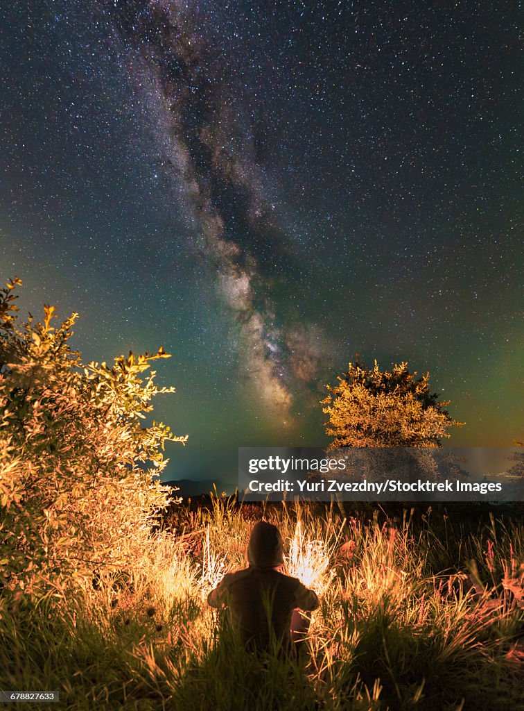 Man sitting near the campfire in the forest under the stars and the Milky Way, Sudak, Crimea.