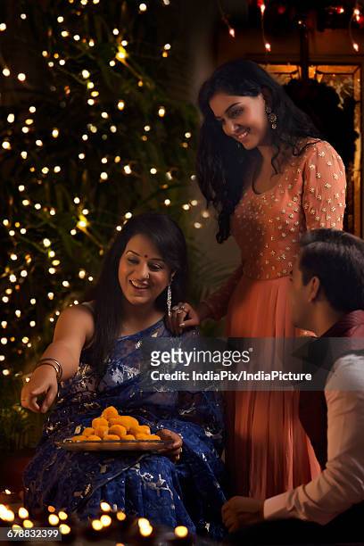 woman with her daughter and son-in-law celebrating diwali - laddoo stock pictures, royalty-free photos & images