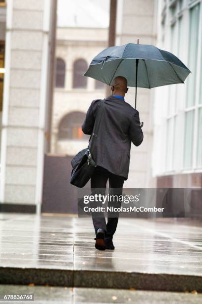 single black businessman heading to work in the rain - homens de idade mediana imagens e fotografias de stock