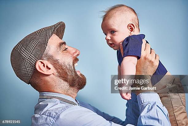 early 30's british male holding infant son in air - happy male side view stock-fotos und bilder