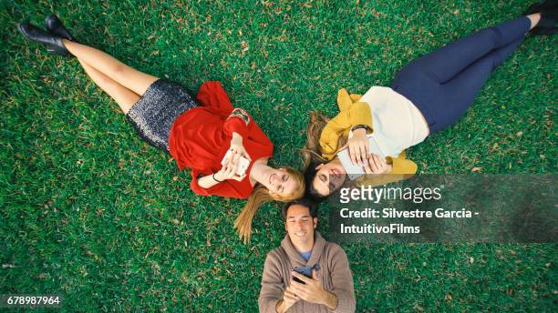 bird´s-eye shot of group of three friends resting over the garden grass - relajación - fotografias e filmes do acervo