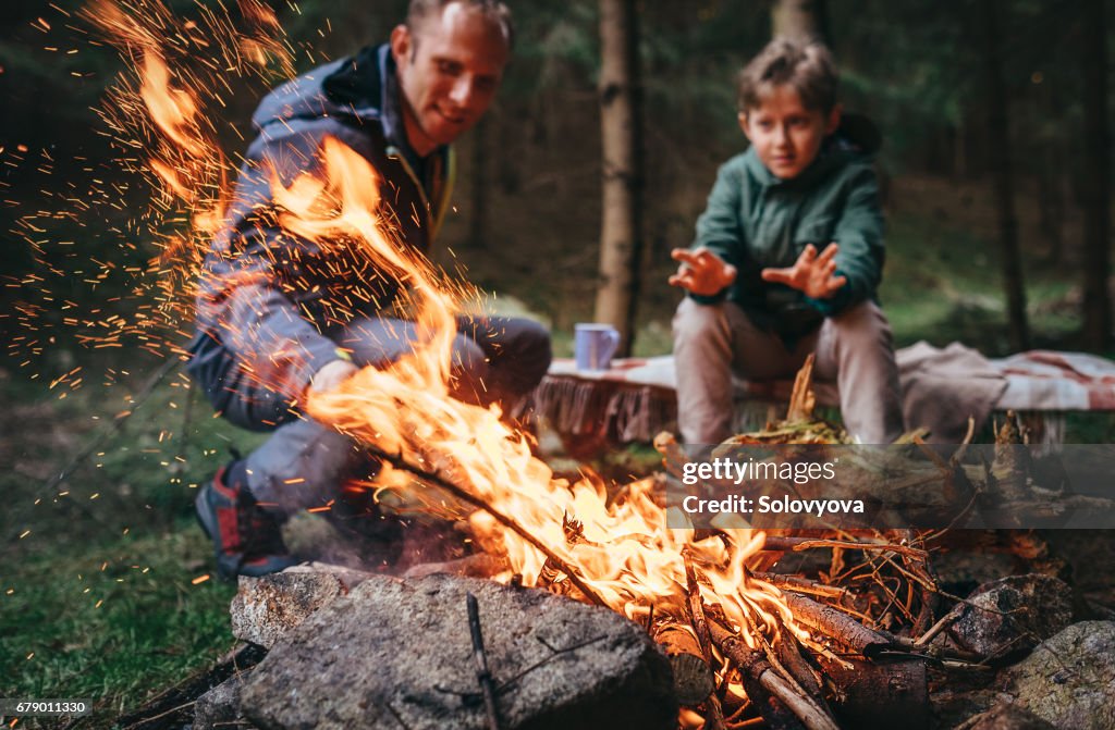 Pai e filho aquece perto da fogueira na floresta