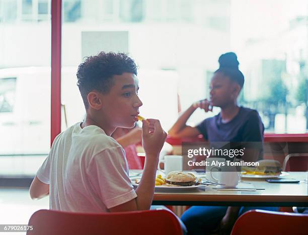 teenage boy in cafe eating burger and chips - fastfood restaurant table stock-fotos und bilder