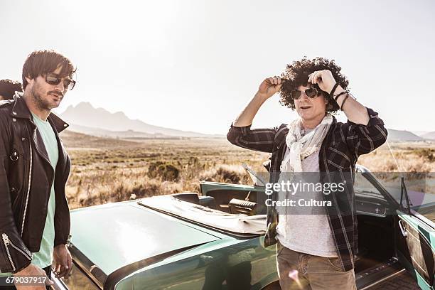male friends on roadside putting on curly wig by convertible, franschhoek, south africa - toyota south africa motors stock pictures, royalty-free photos & images