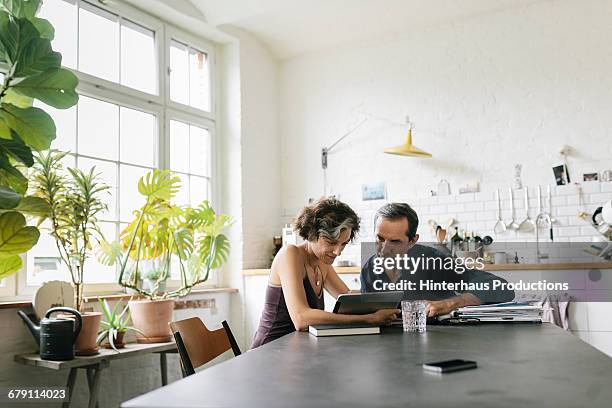 mature couple kisses - couple at table with ipad stockfoto's en -beelden