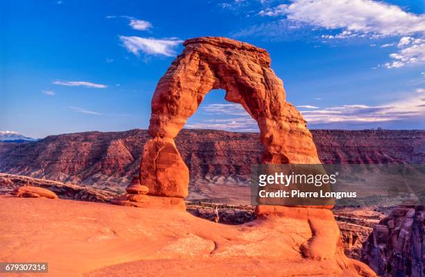 delicate arch with unrecognizable hiker standing under it  - arches national park, utah, usa - arches nationalpark stock-fotos und bilder