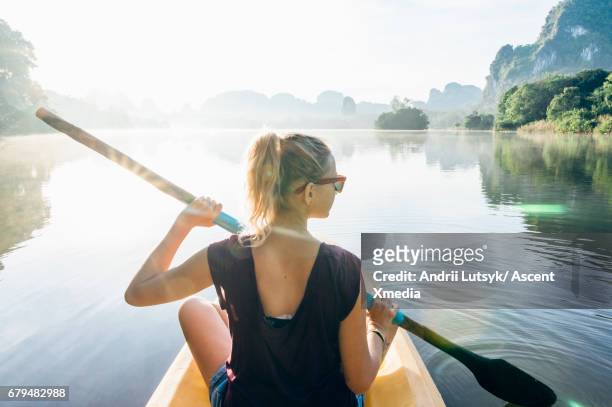 young woman paddles kayak across jungle pond, mountains distant - jungle explorer stock pictures, royalty-free photos & images