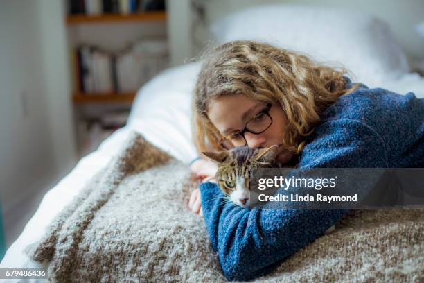 home moments - ein mädchen umarmt ihre gestromte katze auf einem bett - girls cuddling cat stock-fotos und bilder