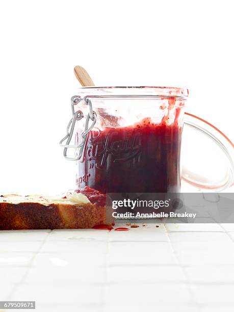 open berry jam mason jar with toast on white tile - strawberry jam stock pictures, royalty-free photos & images