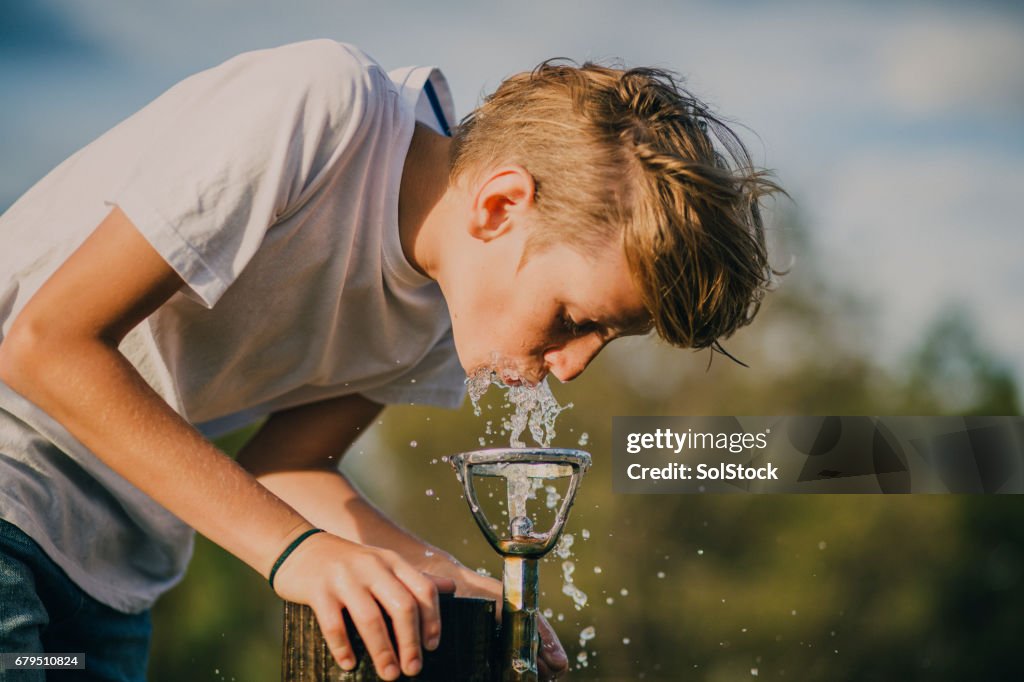 Jovem rapaz bebendo de uma fonte de água