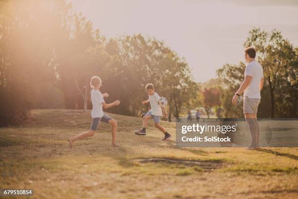 jungs spielen fußball im park - australia football stock-fotos und bilder