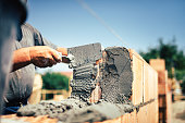 Bricklayer construction worker installing brick masonry on exterior wall with trowel putty knife