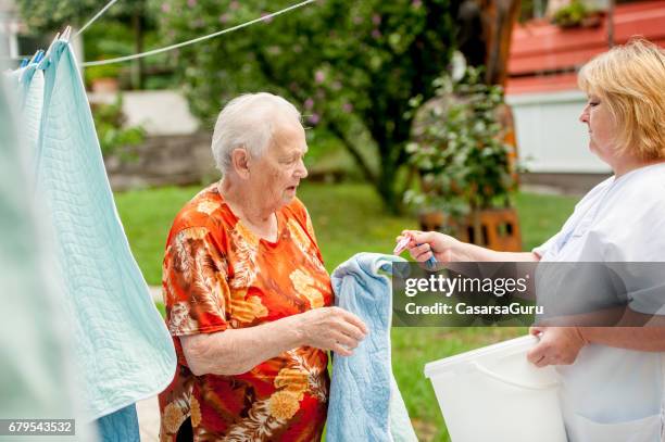 senior woman helping hanging laundry on the washing line at the nursing home - draped blanket stock pictures, royalty-free photos & images