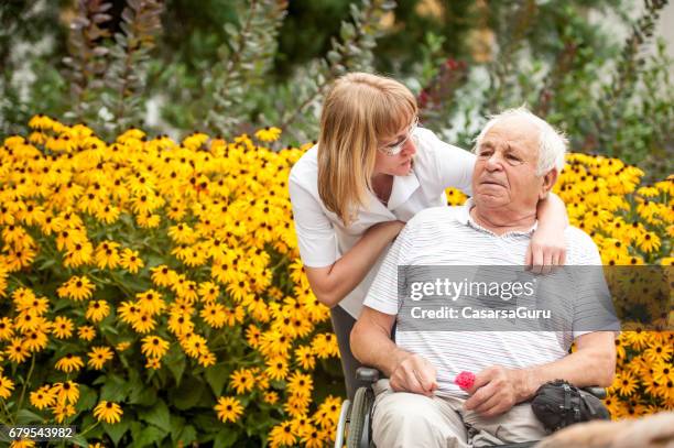 nurse and senior man on wheelchair relaxing in the backyard of the retirement community - memorial garden stock pictures, royalty-free photos & images