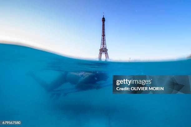 Photo taken from under the water of the Trocadero fountain shows a surfer duck-diving in the water of the fountain, with the Eiffel Tower in the...