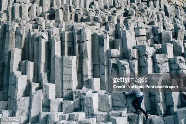 a man climbing basalt columns at black sand beach in iceland - vulkanisch gesteente stockfoto's en -beelden