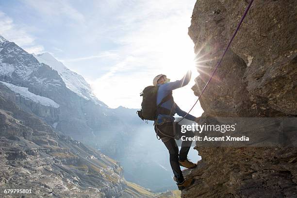 climber ascends vertical cliff above valley below - klettern stock-fotos und bilder