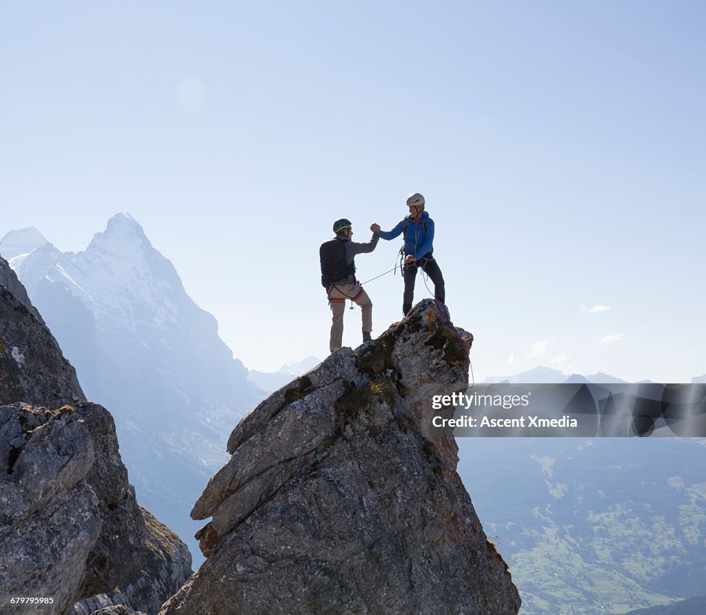 Two climbers exchange handshake on pinnacle summit