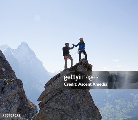 Two climbers exchange handshake on pinnacle summit Two climbers exchange handshake on pinnacle summit
