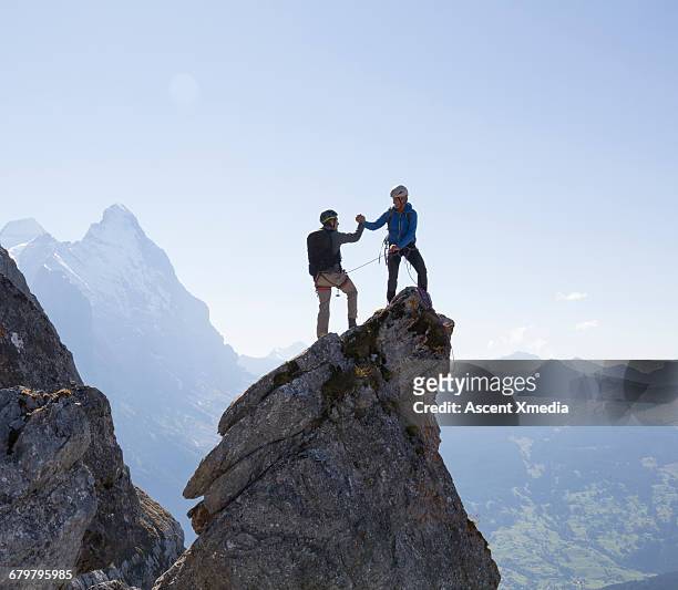 two climbers exchange handshake on pinnacle summit - comemoração conceito imagens e fotografias de stock