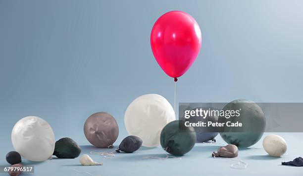 inflated balloon surrounded by deflated balloons - blowing up balloon stock pictures, royalty-free photos & images