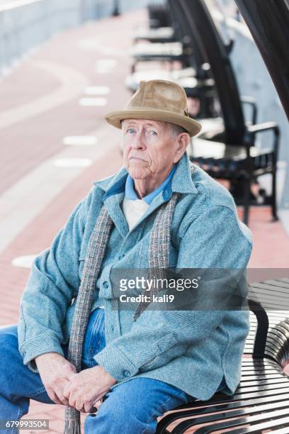 fatigué de vieil homme assis sur un banc, fronçant les sourcils - vieux grincheux photos et images de collection