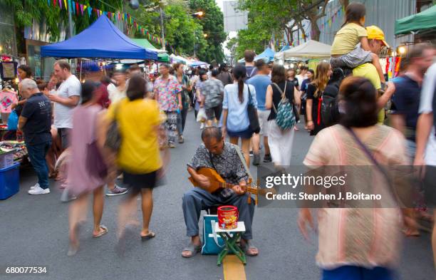 People walk past a man playing a guitar at the Sunday Night Market on Rachadamnoen Rd in Chiang Mai, Thailand.