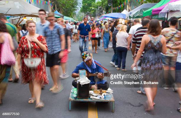 People walk past a man playing a guitar at the Sunday Night Market on Rachadamnoen Rd in Chiang Mai, Thailand.
