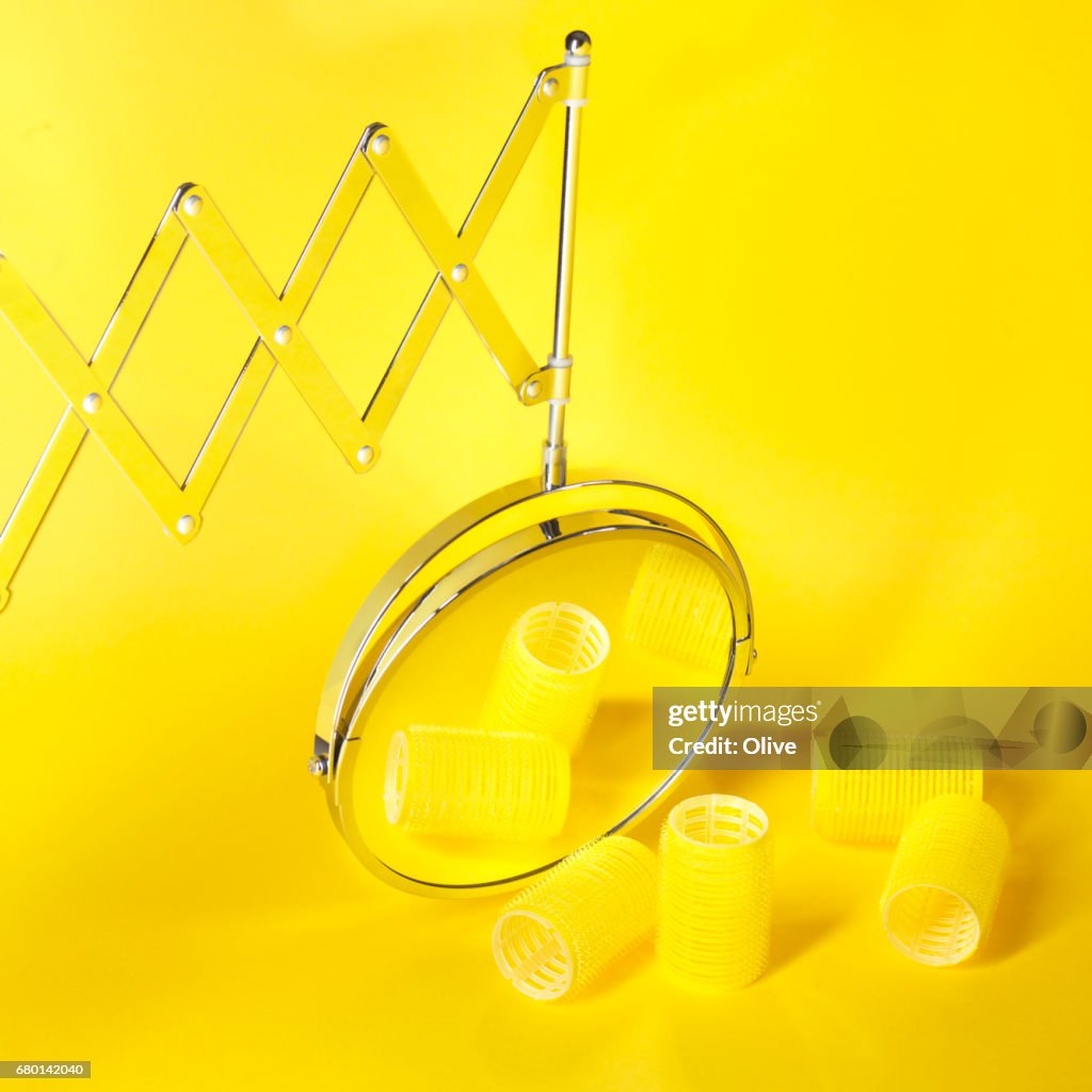 Magnifying mirror on yellow background with rollers