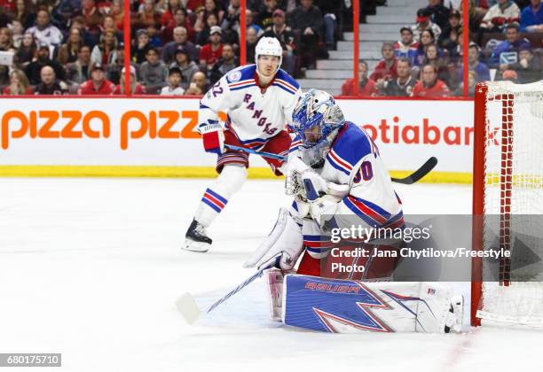 Henrik Lundqvist of the New York Rangers has the puck go under his throat guard as he makes a save and teammate Nick Holden looks on in overtime in...