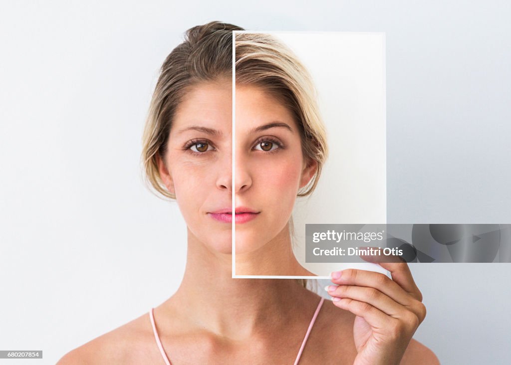 Middle age woman holding photo of face when she was younger