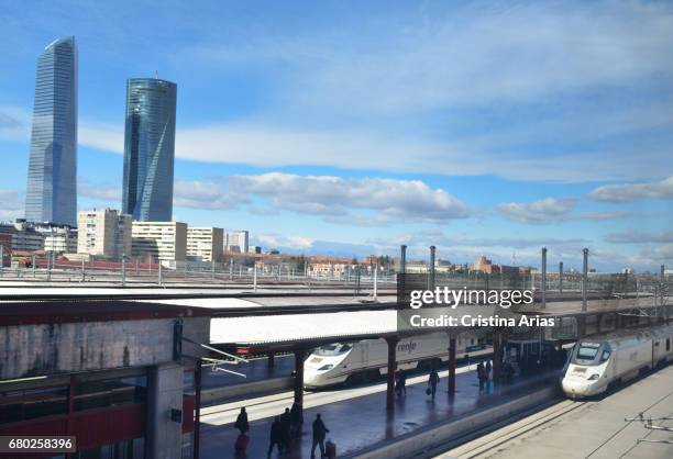 Passengers next to the high speed trains standing on the platforms of the train station of Chamartin and in the background the skyscrapers of the our...