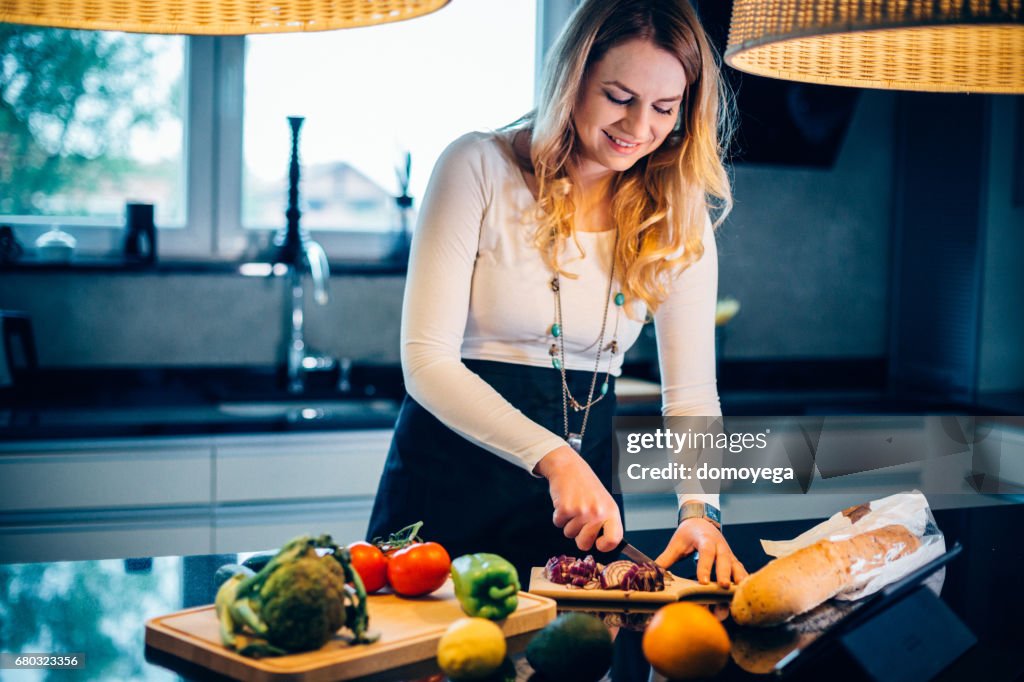 Young woman cutting onion and preparing food in the kitchen