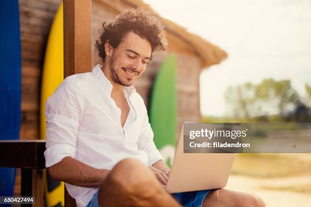 attractive man using a laptop at a beach bar - sunlit cafe male stock pictures, royalty-free photos & images