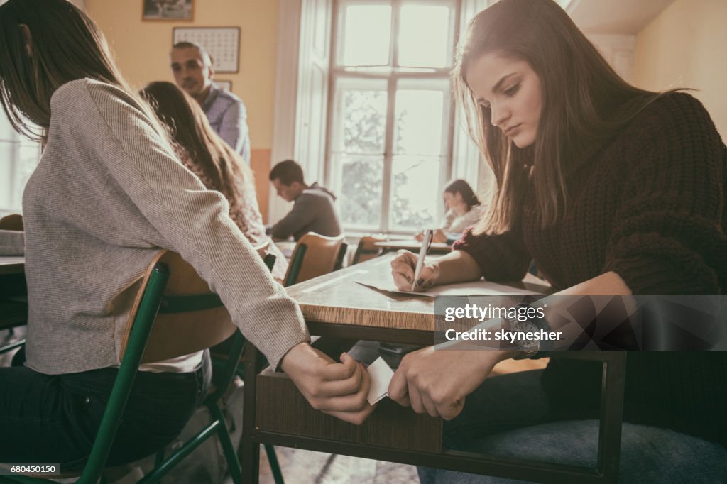 Two High School Students Passing Note During The Exam In The Classroom two-high-school-students-passing-note-during-the-exam-in-the-classroom